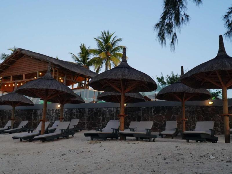 Pláž s lehátky a slaměnými slunečníky před dřevěnou chatkou za soumraku.