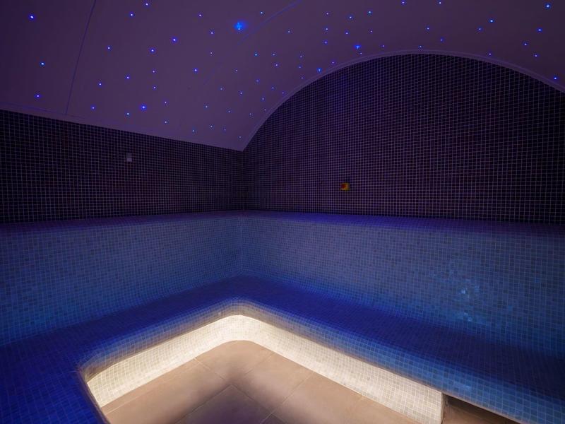 Osvětlené moderní vnitřní jacuzzi s hvězdnou oblohou na stropě.