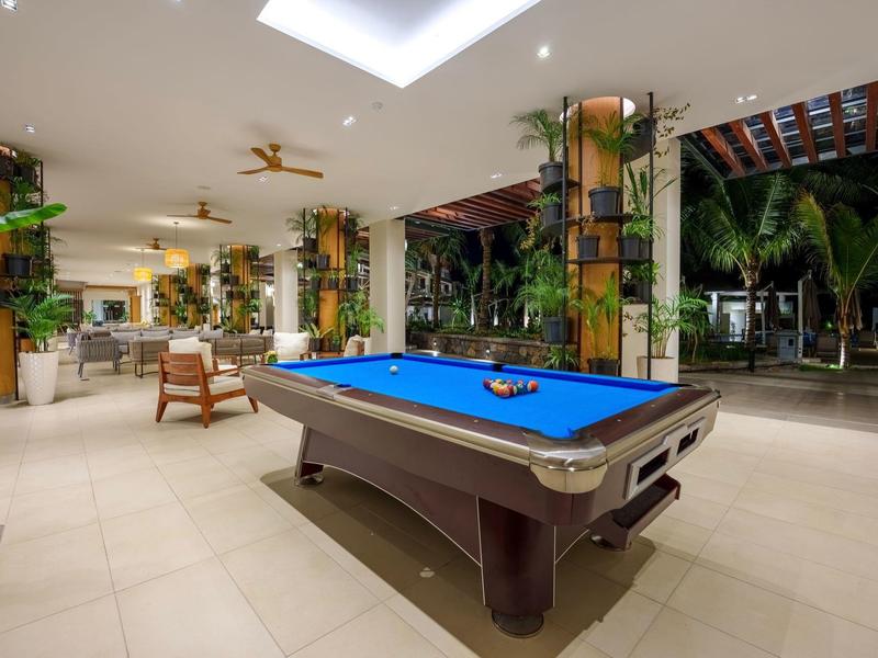 Moderní odpočinková místnost s modrým kulečníkovým stolem a tropickými rostlinami v pozadí.