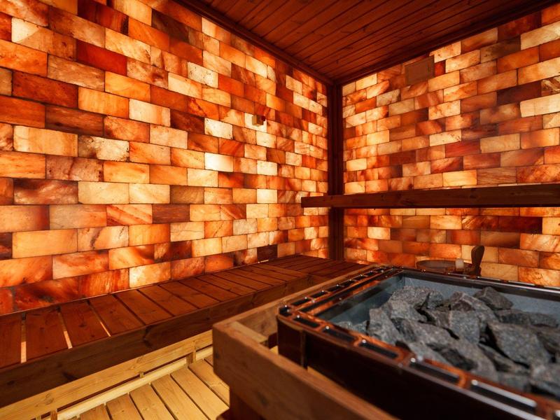 Moderní solná sauna s teplými dřevěnými lavicemi a zářícími stěnami z kamene soli.