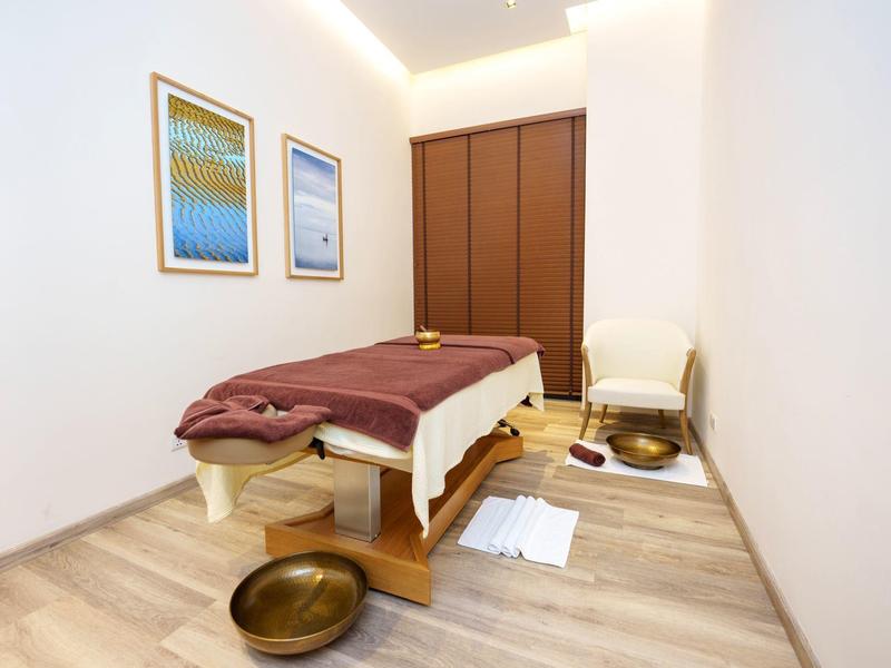 Klidná masážní místnost s lehátkem, uklidňujícím osvětlením a měděnými miskami.
