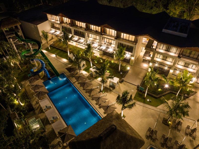 Noční pohled na osvětlený hotel s bazénem a zahradou.