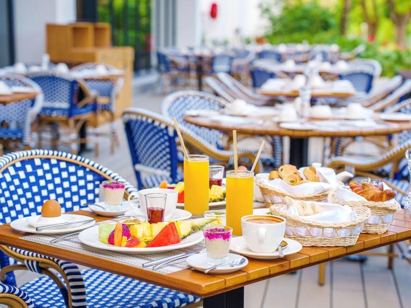 Snídaňový stůl s čerstvým ovocem, džusy, kávou a pečivem na terase s modrými židlemi.