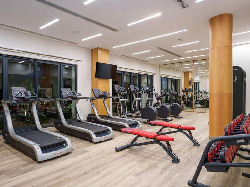 Moderní posilovna s běžeckými pásy, lavicemi na cvičení a velkými okny v hotelu.