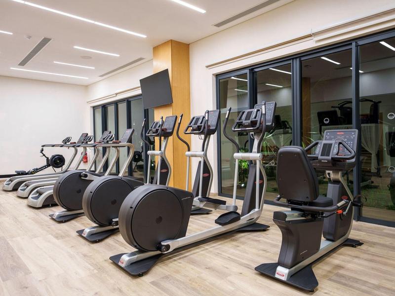 Moderní fitness stroje v světlé tělocvičně s velkými okny.