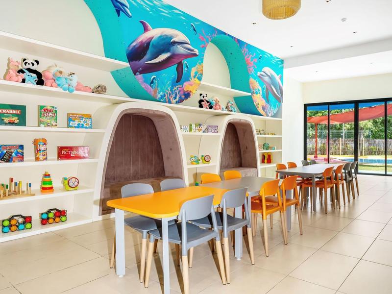 Světlá dětská herna s barevným nástěnným malbou delfínů, stoly a barevnými židlemi.