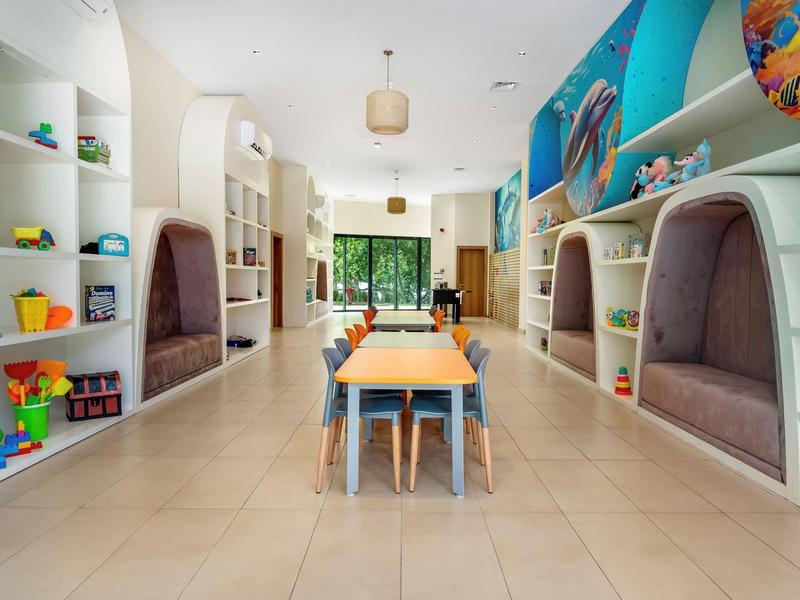Světlá dětská herna v hotelu s stoly, židlemi, hračkami a útulnými nikami pro děti