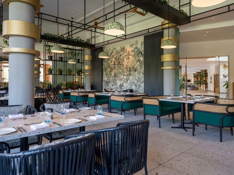 Moderní restaurace se zelenými čalouněnými lavicemi a elegantně prostřenými stoly.