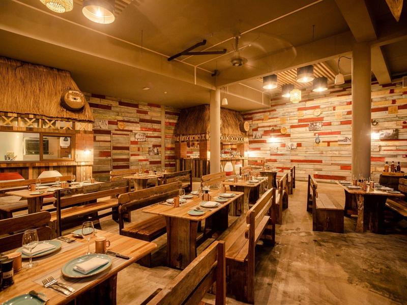 Rustikální restaurace s dřevěnými stoly a teplým, barevným osvětlením stěn.