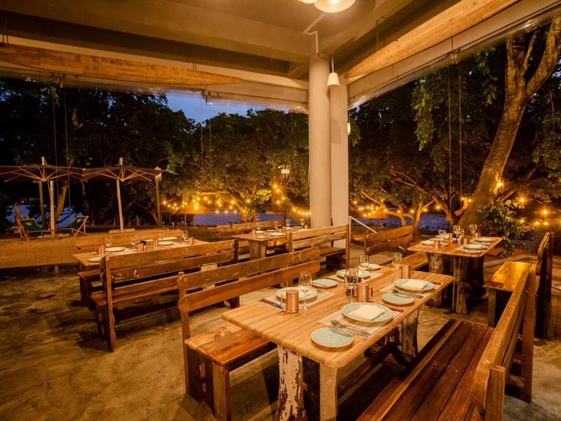 Pohodlná venkovní část restaurace s dřevěnými stoly a teplými světelnými řetězy za soumraku.