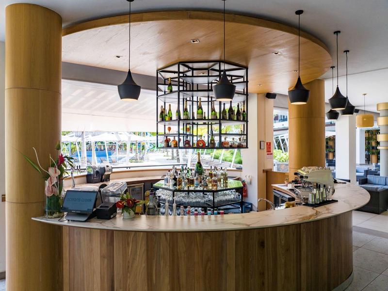 Moderní hotelový bar s kulatým dřevěným pultem a závěsnými policemi nad barem.