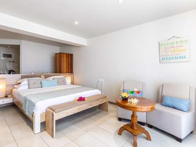 Jasně zařízený hotelový pokoj s manželskou postelí, pohodlným křeslem a kulatým dřevěným stolem.