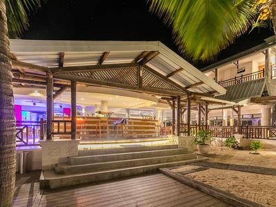 Beleuchtete Hotelbar mit überdachter Terrasse und Palmen bei Nacht.