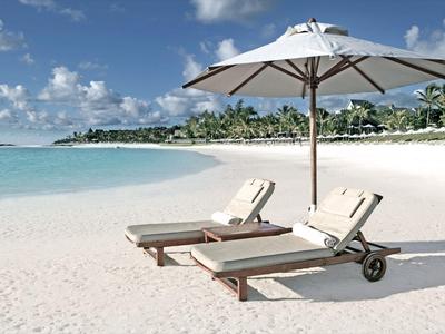 Zwei Liegestühle unter Sonnenschirm am weißen Sandstrand mit türkisfarbenem Meer im Hintergrund.