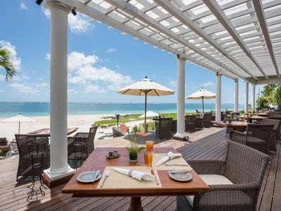 Terrasse mit gedeckten Tischen, Sonnenschirmen und Blick auf den Strand und das Meer.