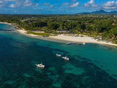 Pláž s čistou vodou, loděmi na moři a zalesněným pobřežím pod slunečnou oblohou.