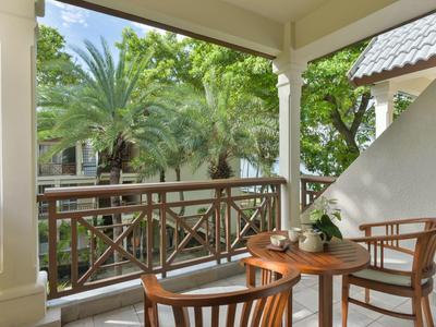 Balkon s dřevěným stolem a židlemi s výhledem na palmy a zelené listí.