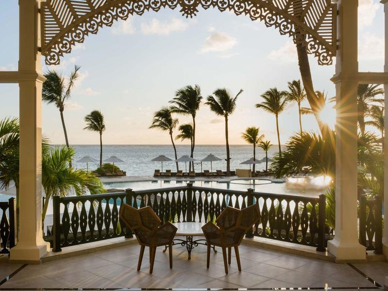 Výhled z verandy na palmy, moře a západ slunce se dvěma židlemi v popředí.