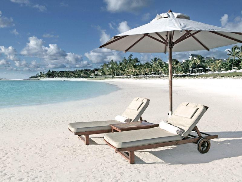 Dva plážové lehátka s bílým slunečníkem na písečné pláži u tyrkysového moře.