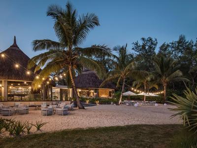 Plážové resort s palmami, lehátky a osvětlenou restaurací za soumraku.