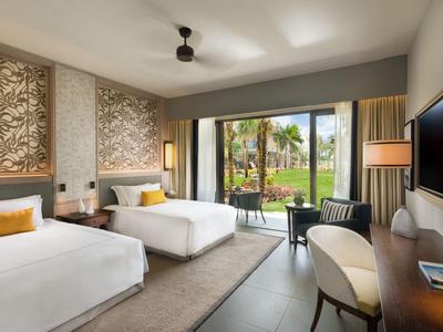 Moderní hotelový pokoj se dvěma postelemi, pracovním stolem a výhledem na zahradu přes velké posuvné skleněné dveře.