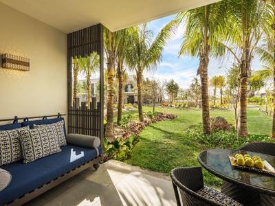 Pohodlná terasa s modrou pohovkou a stolem s výhledem na tropickou zahradu s palmami.