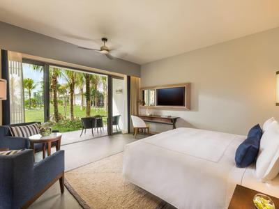 Světý hotelový pokoj s otevřeným balkonem s výhledem na palmy a zahradu.