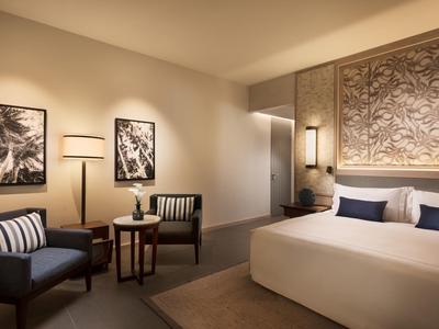 Elegantní hotelový pokoj s velkou postelí, křesly a dekorativními obrazy na stěně.