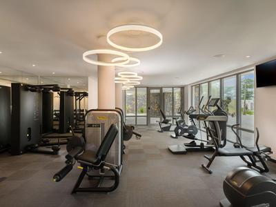 Moderní fitness s různými posilovacími stroji a velkými okny.