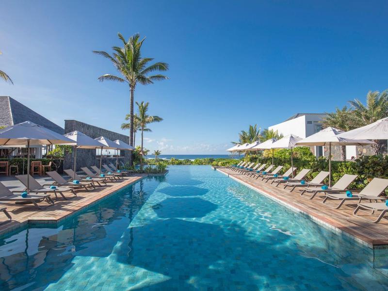 Dlouhý venkovní bazén s lehátky a palmami pod jasně modrou oblohou v hotelu