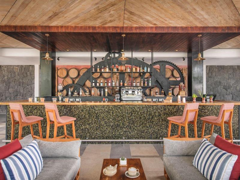 Moderní hotelový bar s dřevěným stropem, oranžovými židlemi a útulnými posezeními.