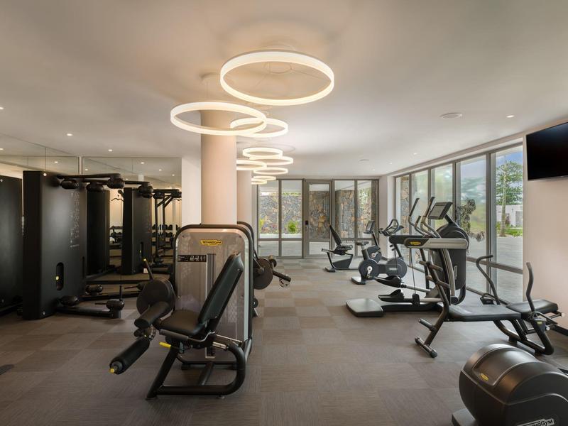 Moderní posilovna s velkými okny a stylovými kruhovými světly na stropě.