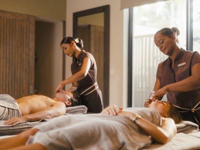 Twee vrouwen krijgen massages van therapeuten in een rustige spa met natuurlijk licht.