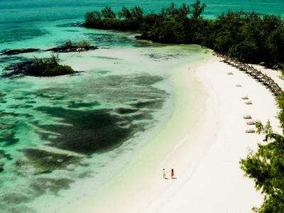 Een tropisch strand met helder turquoise water, wit zand en weelderig groen langs de kust.