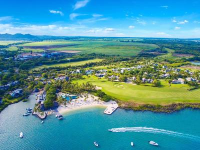 Kuststad met strand, boten op helder blauw water en groene velden onder een deels bewolkte hemel.