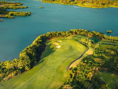 Een weelderige golfbaan omgeven door water en bomen onder een bewolkte lucht.