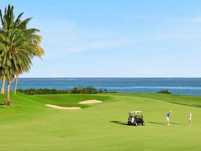 Grüner Golfplatz am Meer mit zwei Golfern und Golfwagen bei klarem Himmel.