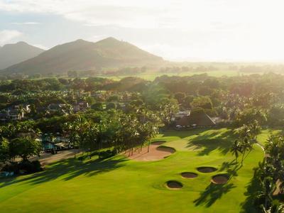 Zonnige golfbaan met weelderig groen en bergen in de verte onder een gedeeltelijk bewolkte hemel.