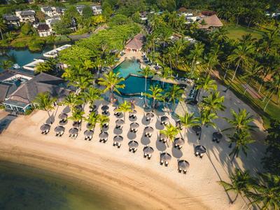 Vogelperspektive eines Resorts mit Strand, Liegestühlen und großem Pool umgeben von Palmen.
