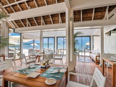 Licht restaurant aan zee met houten meubels en tropisch uitzicht door grote ramen.