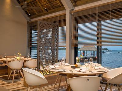 Gezellige eetruimte met ronde tafels en stoelen bij ramen met uitzicht op zee.