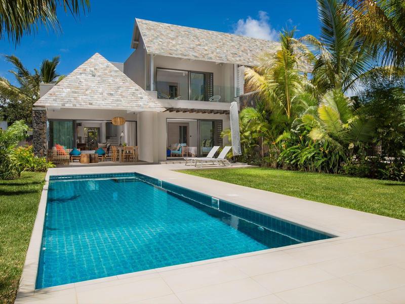 Twee verdiepingen tellend huis met zwembad en weelderige tuin onder een heldere blauwe lucht.