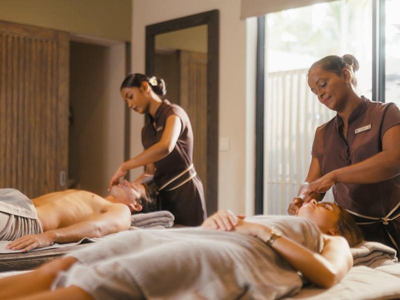Twee vrouwen krijgen massages van therapeuten in een rustige spa met natuurlijk licht.