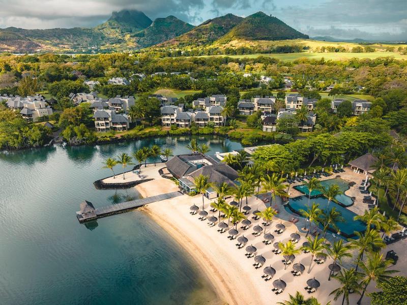Luchtfoto van een tropisch resort met strand, zwembad en groene bergen op de achtergrond.