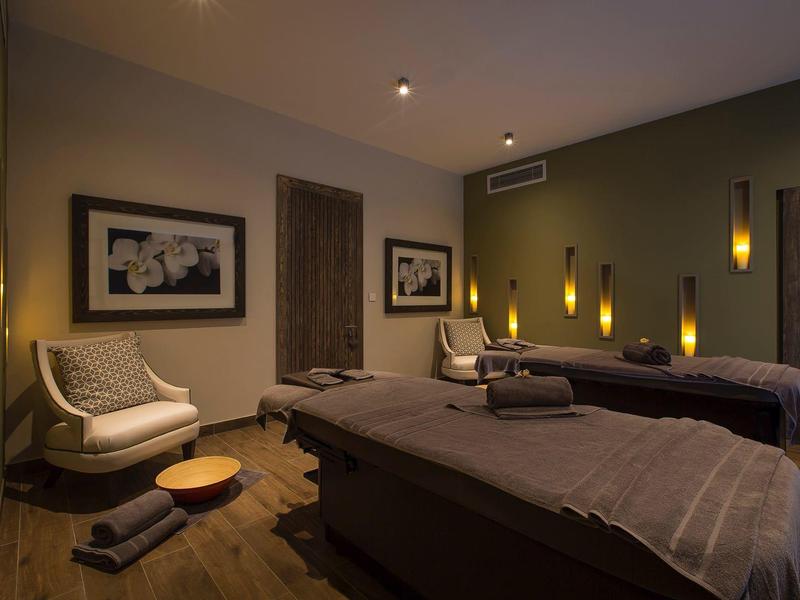 Rustige spa kamer met twee massagetafels, fauteuils, zachte verlichting en kalmerende decoratie.