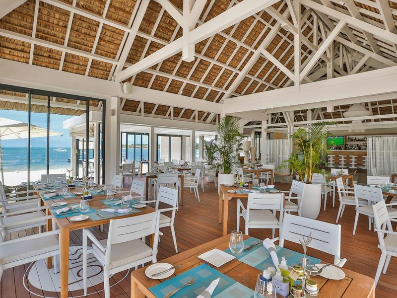 Ruim restaurant aan het strand met witte houten stoelen, tafels en een hoog zadeldak met zichtbare balken.