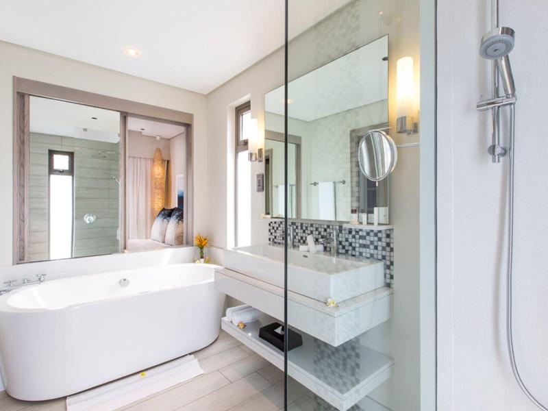 Lichte moderne badkamer met bad, glazen douche, grote spiegel en witte wastafel.