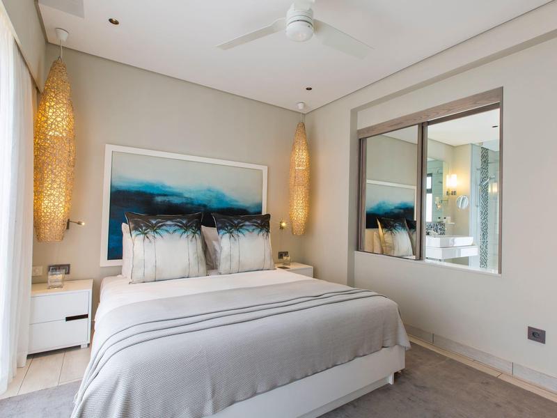 Moderne slaapkamer met tweepersoonsbed, abstract hoofdeinde, zachte verlichting en grote spiegel.