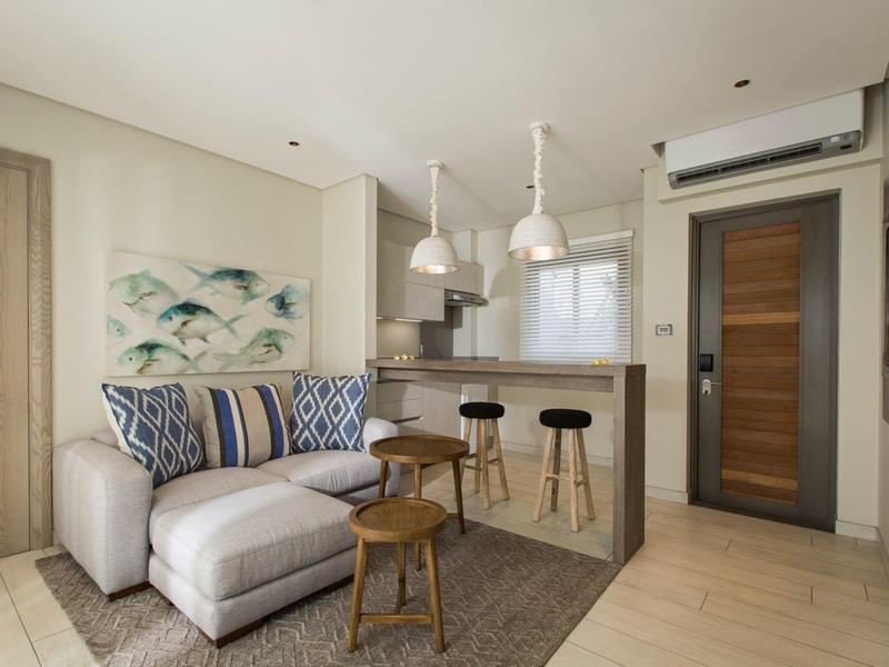 Moderne woonkamer met beige bank, houten krukken en een keukenbar onder hanglampen.