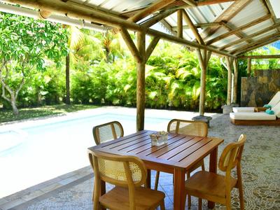 Area esterna coperta con tavolo in legno, sedie e sdraio accanto a una piscina.